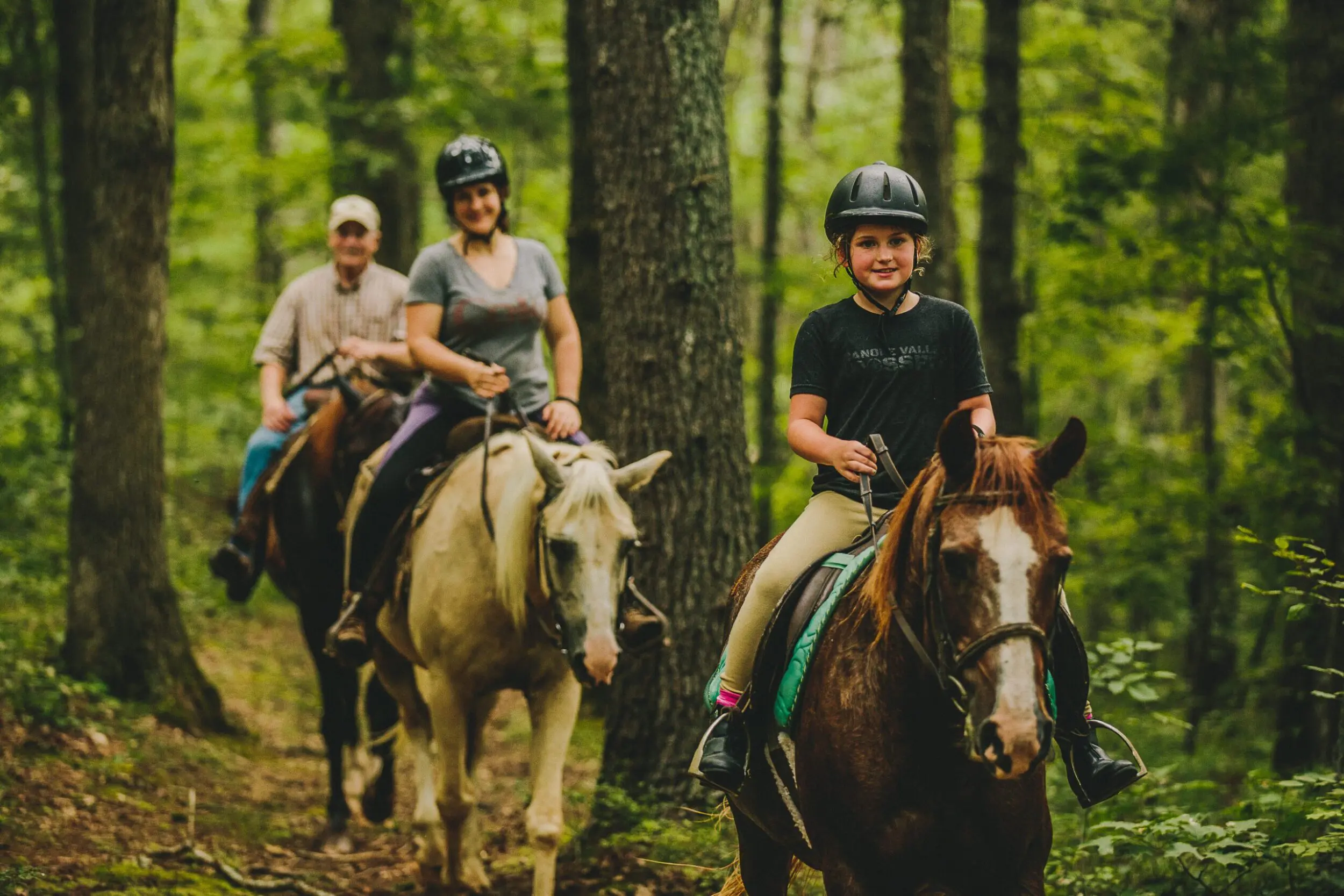 A young girl horseback rides through the woods with two adults riding behind her in Botetourt County, VA