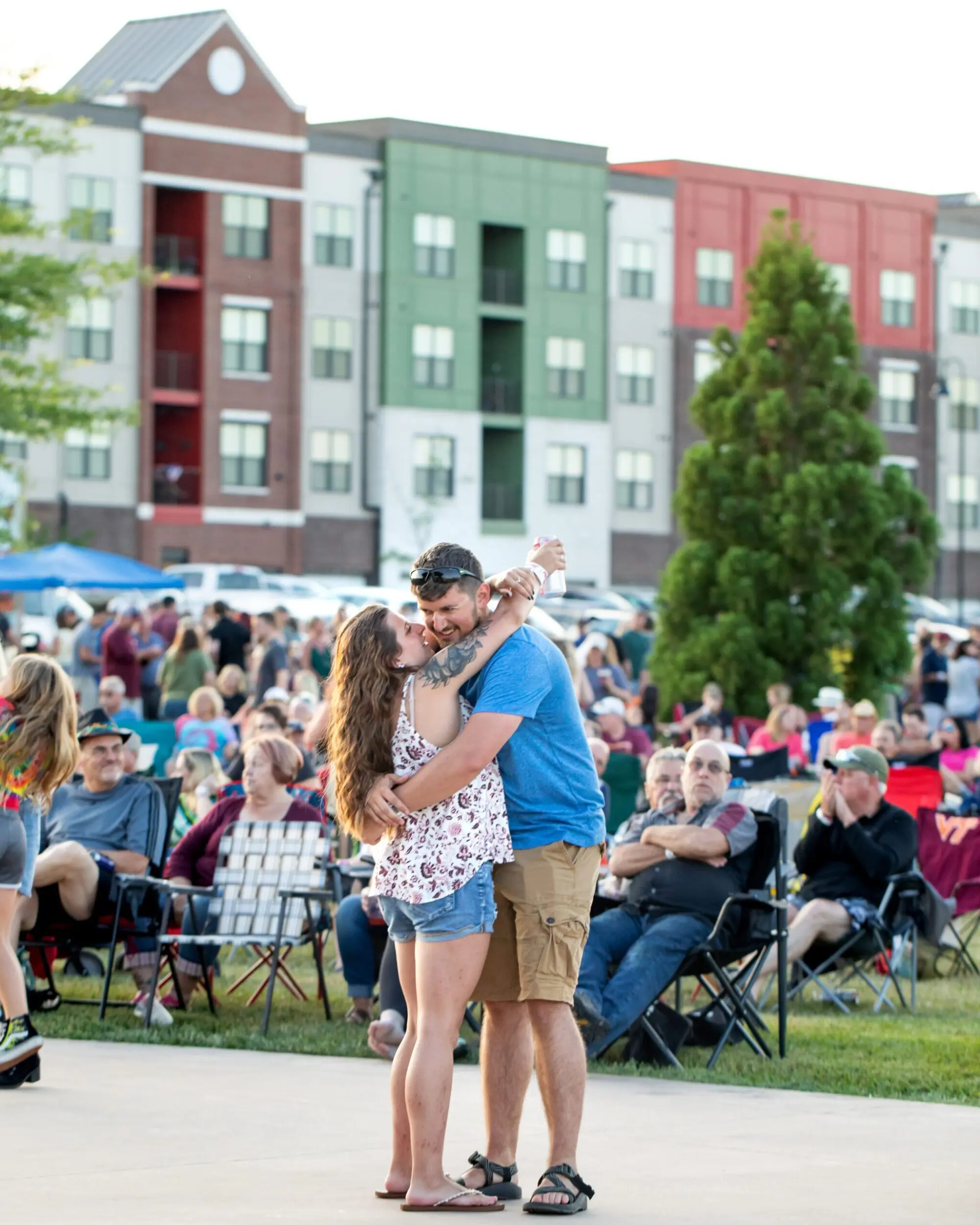 Two young adults dance in front of the Daleville Town Center apartments at an outdoor event. In the background is a large crowd of people seated and looking toward something out of frame.