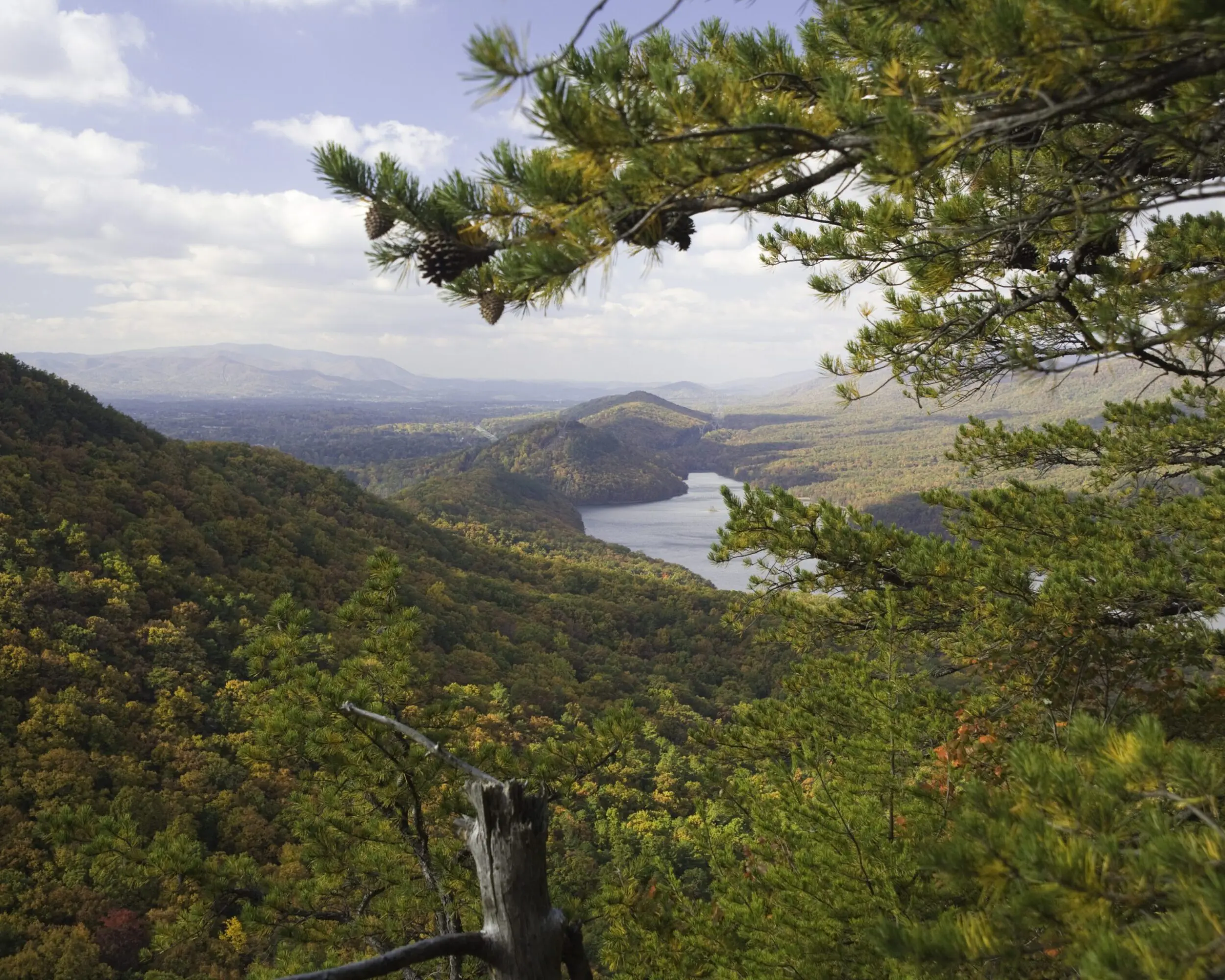 View from the top of Tinker Mountain as it overlooks Carvins Cove in Botetourt County. The mountains are covered in trees with green, orange, and yellow leaves.