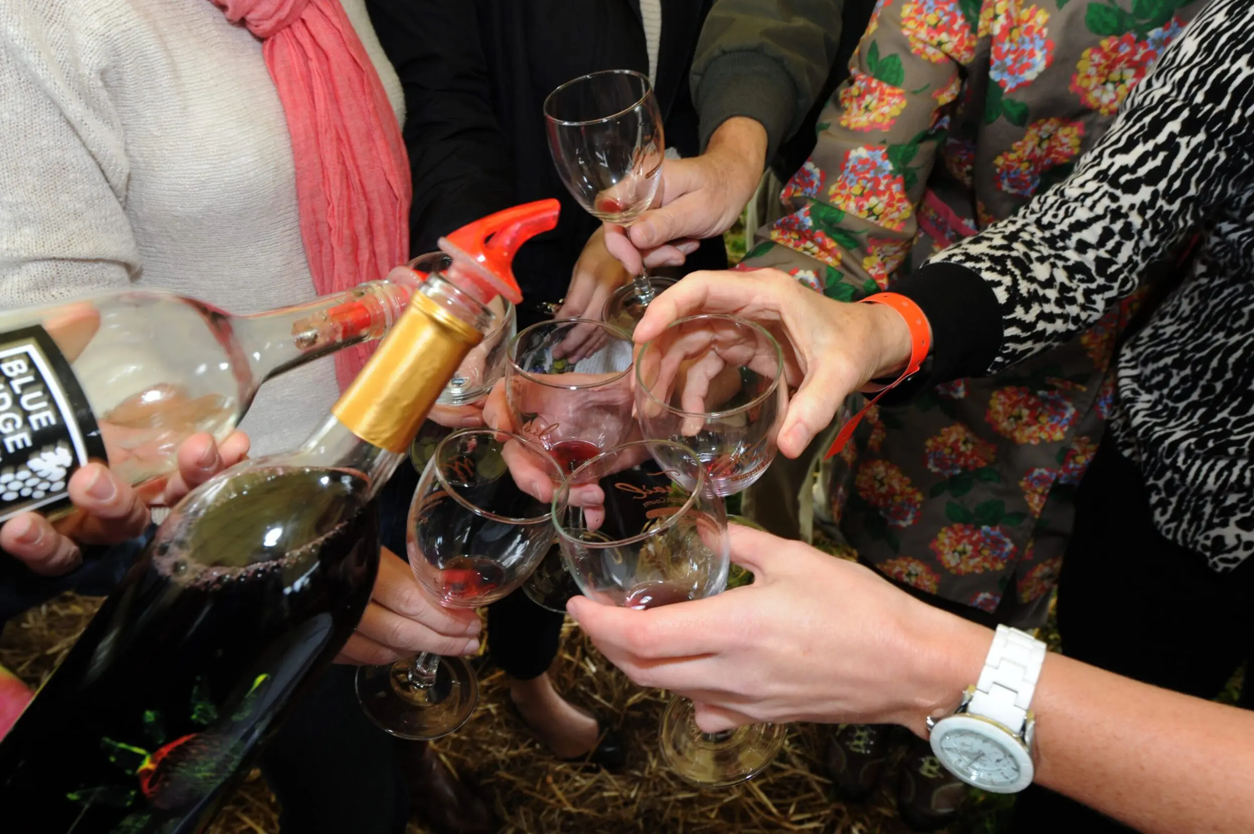 Several people placing their glasses together as someone pours more wine into them.