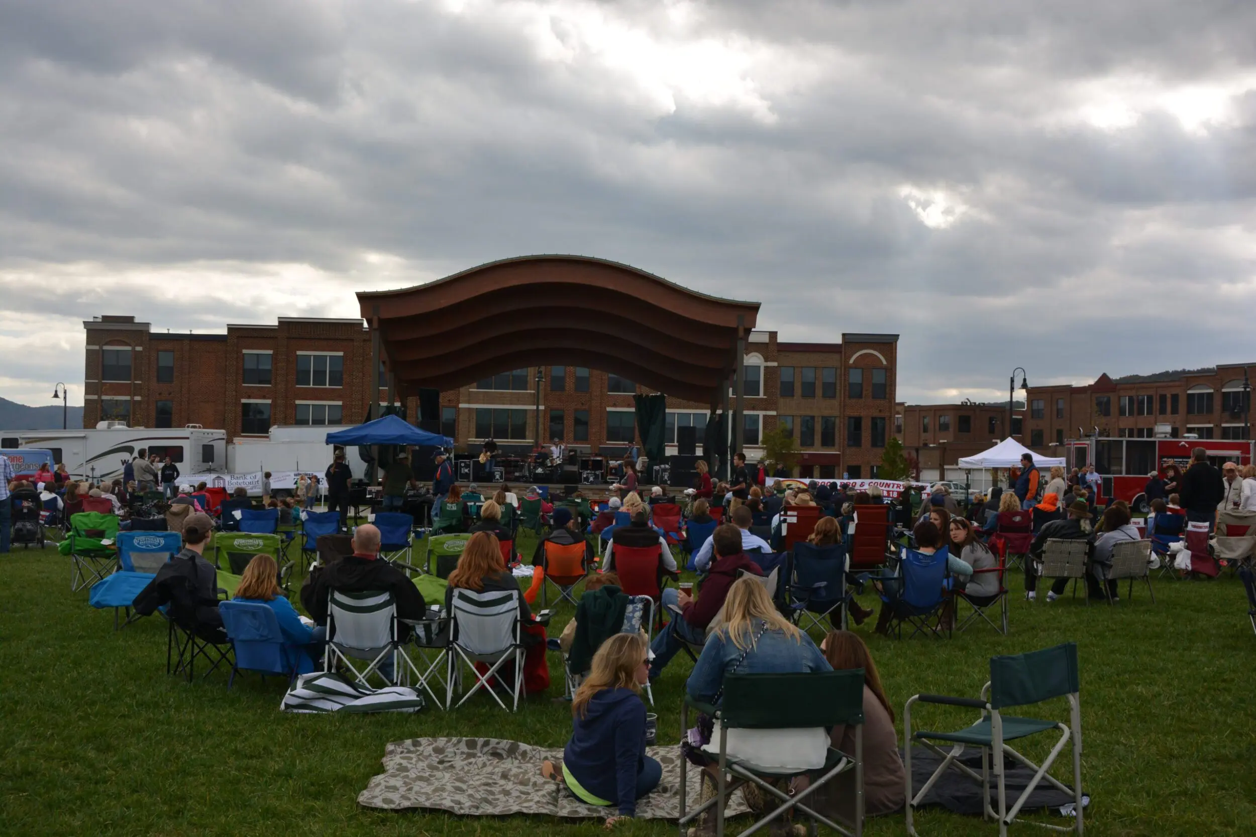 Overcast evening at the Daleville Town Center at a concert. There is a crowd of people seated in lawn chairs as they face an outdoor amphitheater.