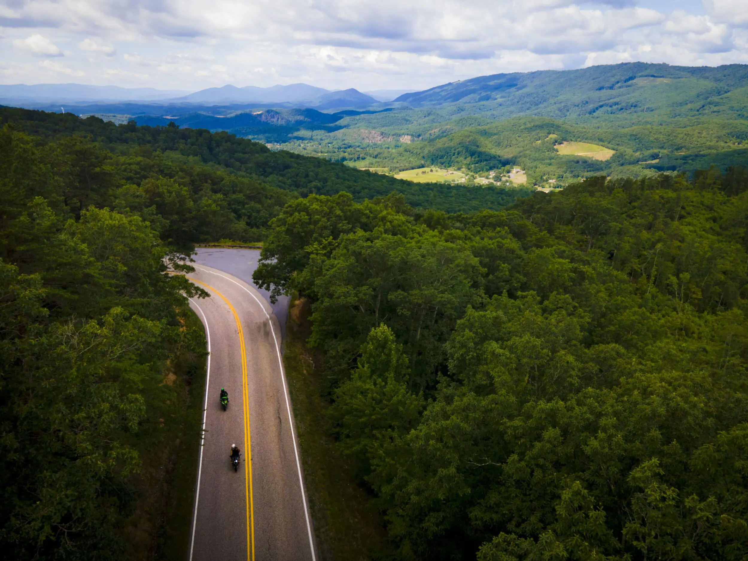 Aerial shot of street through the Allegheny Mountains. It's a sunny, summer day with lush, green trees covering the mountains.