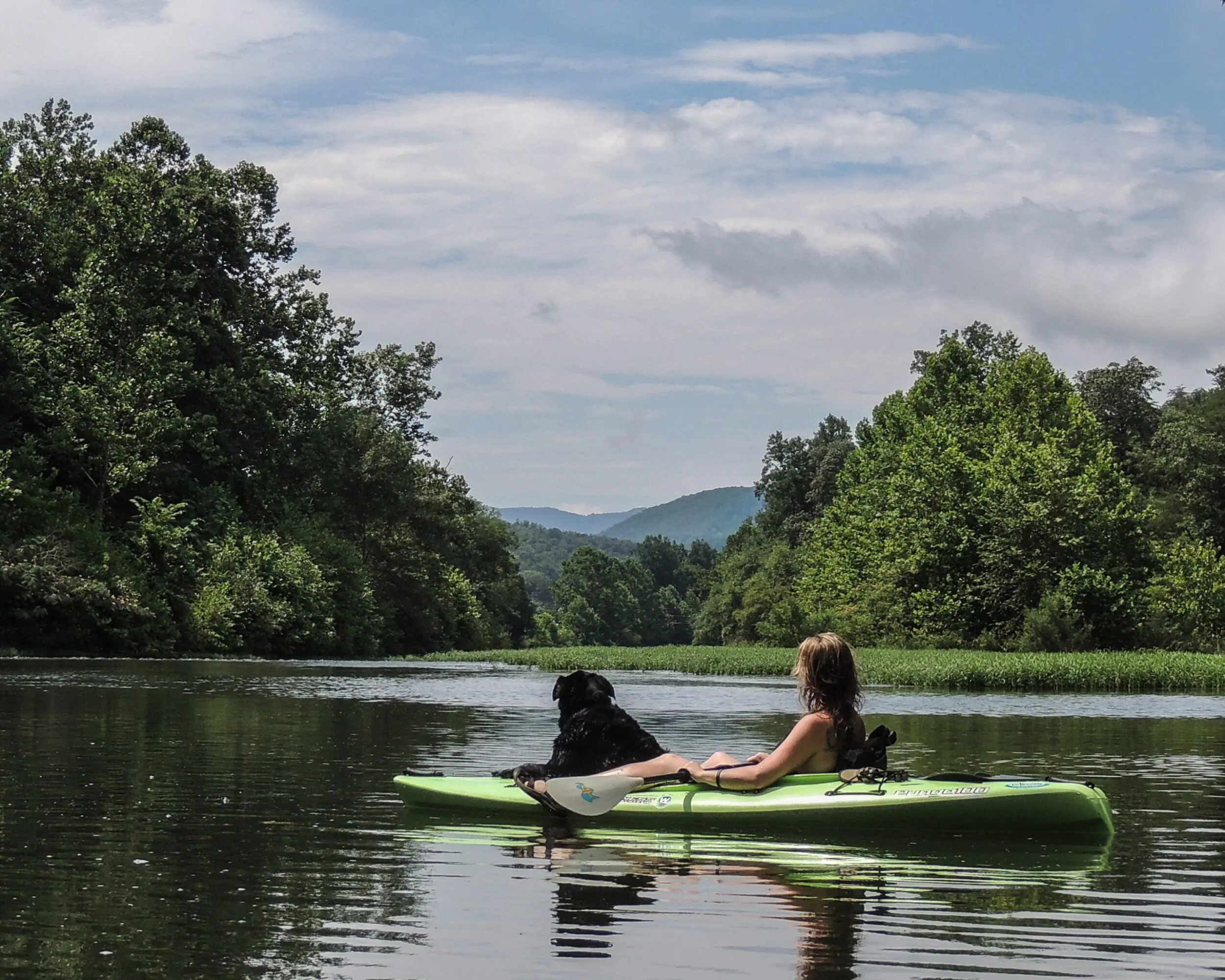 young, white woman and her large black dog relax on a kayak on the Cowpasture River in Alleghany County in Virginia.