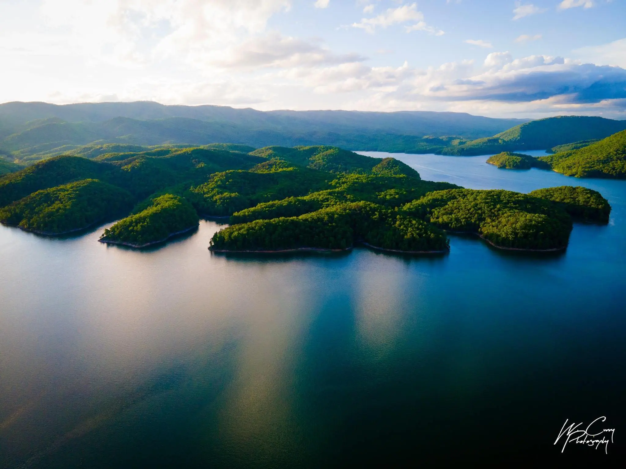 Aerial shot of Lake Moomaw on a beautiful summer day during golden hour. The lake is lined with mountains with green lumpy peninsulas in the water.