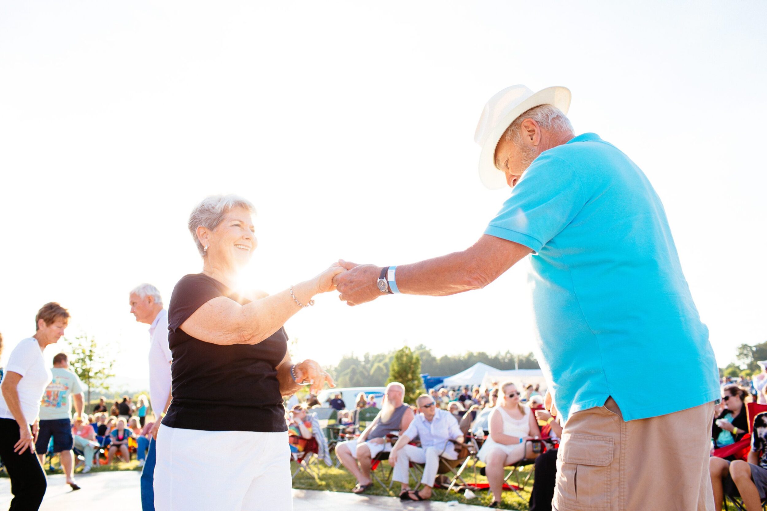 An older white couple in their early sixties dance at an outdoor concert in Botetourt County, VA. It's a sunny day, and they smile at one another as other attendees look on.