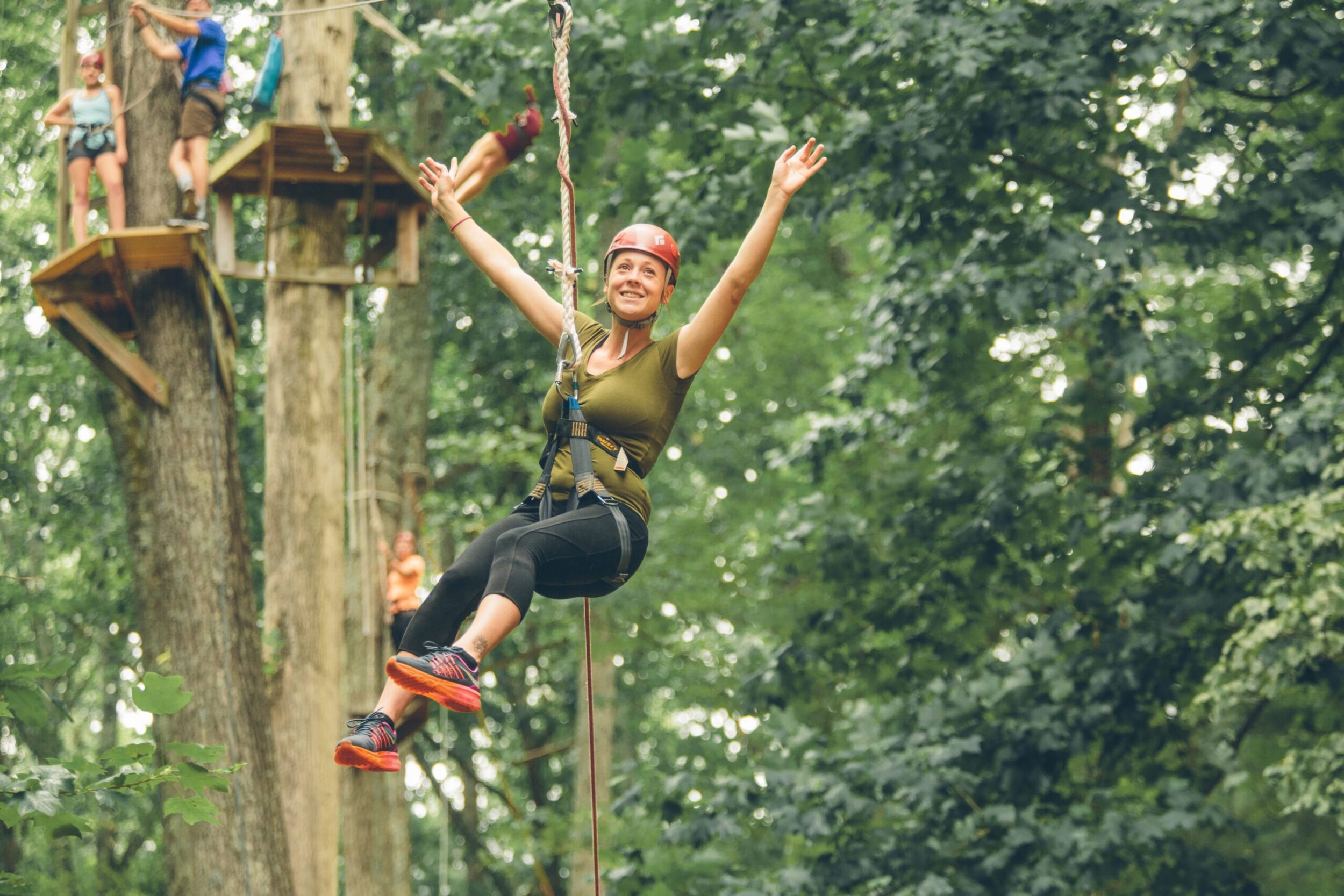 A young white woman smiles and raises her arms above her head as soars across a zipline at Treetop Quest in Explore Park in Roanoke County, VA.