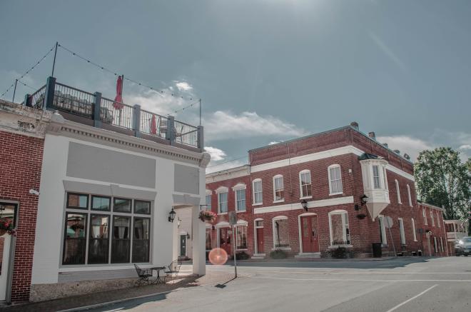 View of 1772 Rooftop bar and restaurant in Fincastle, VA with other quaint, red brick shops. It's a bright sunny day.