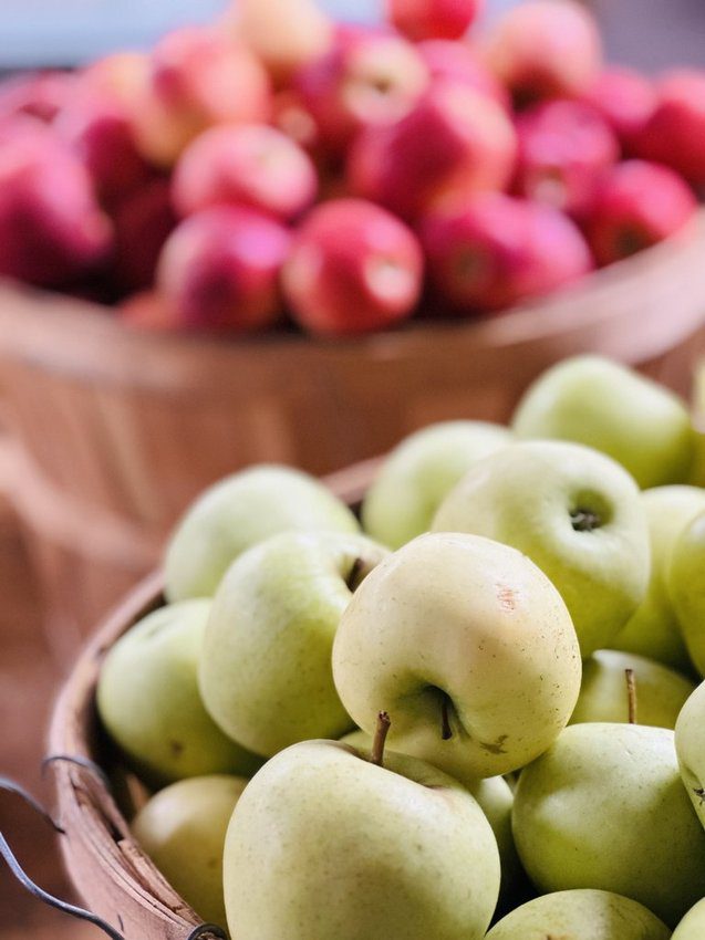 A barrel of green apples in the foreground and a barrel of red apples in the background.