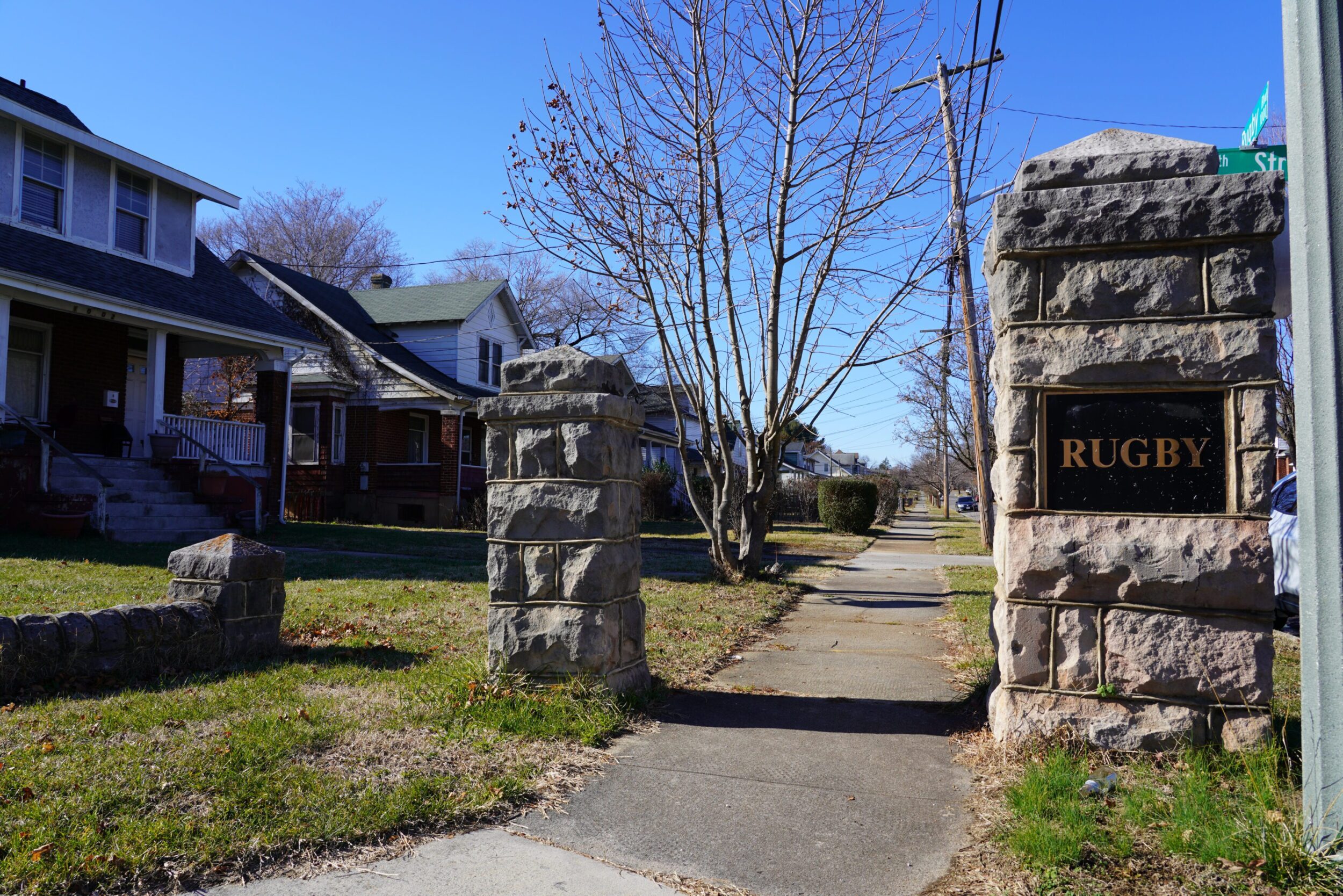 Stone pillars at the corner of a neighborhood entrance. The pillar on the right holds a plaque that reads "Rugby" for the Melrose-Rugby nieghborhood.