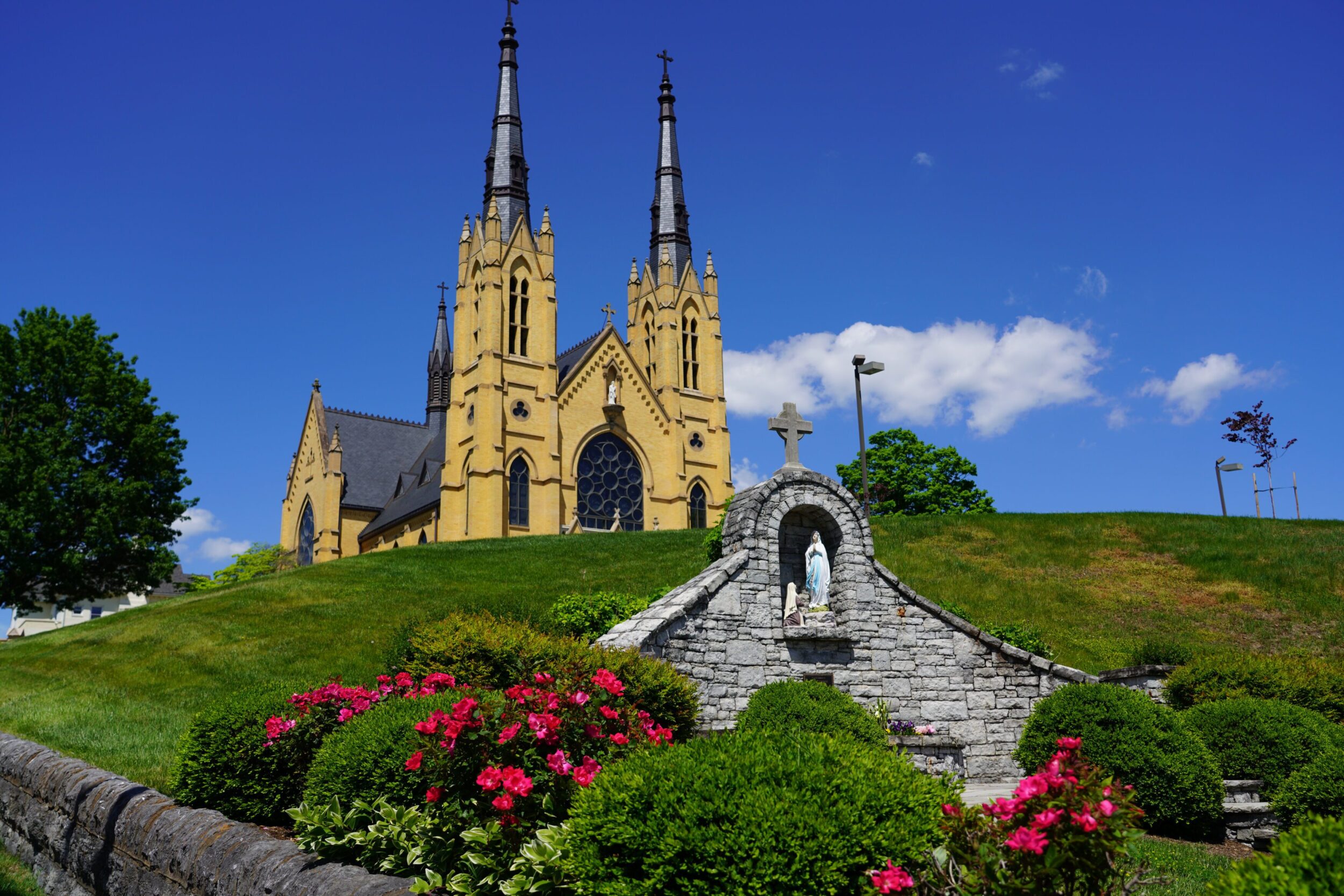 Exterior photo of Saint Andrew's Catholic Church in Roanoke, VA. It is yellow in color with two large spires reaching into the blue sky.