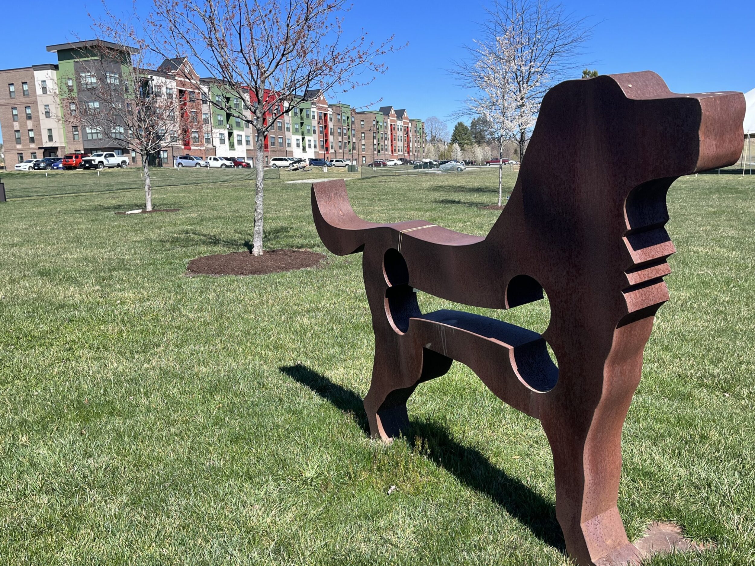 A metal cut-out of a dog at the dog park at the Daleville Town Center. In the background, there are colorful apartments in the background on a sunny spring day.