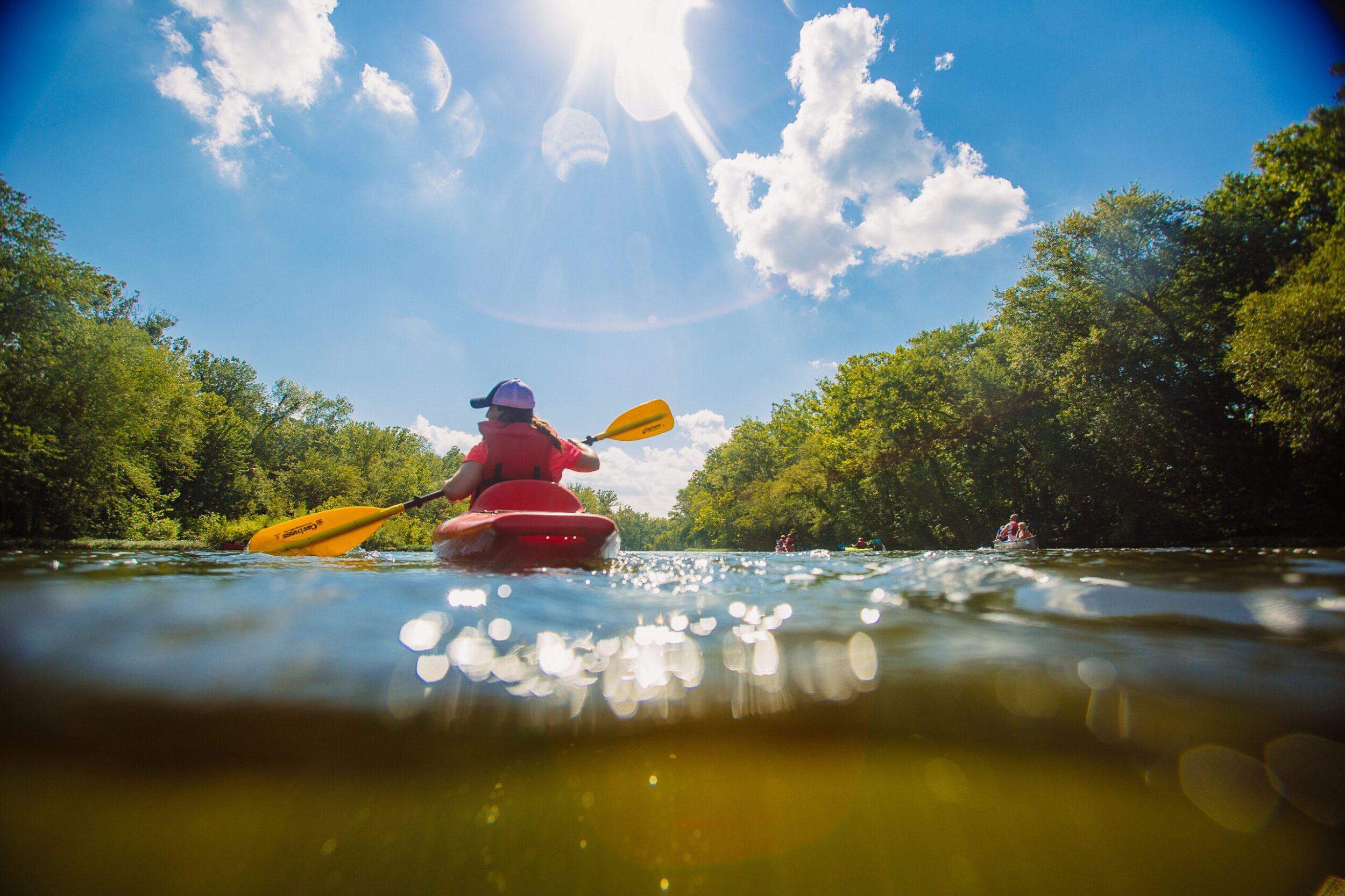 White female in a kayak paddles away from the camera. It's a beautiful, sunny day on the James River in Botetourt County, VA.