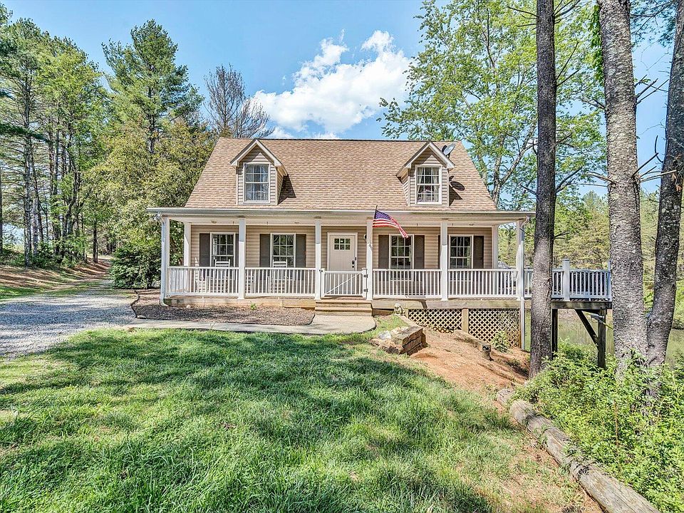 Cape Cod brick home with a covered front porch and an American flag hanging off the porch. It's a sunny day, and the house is surrounded by tall, green trees.