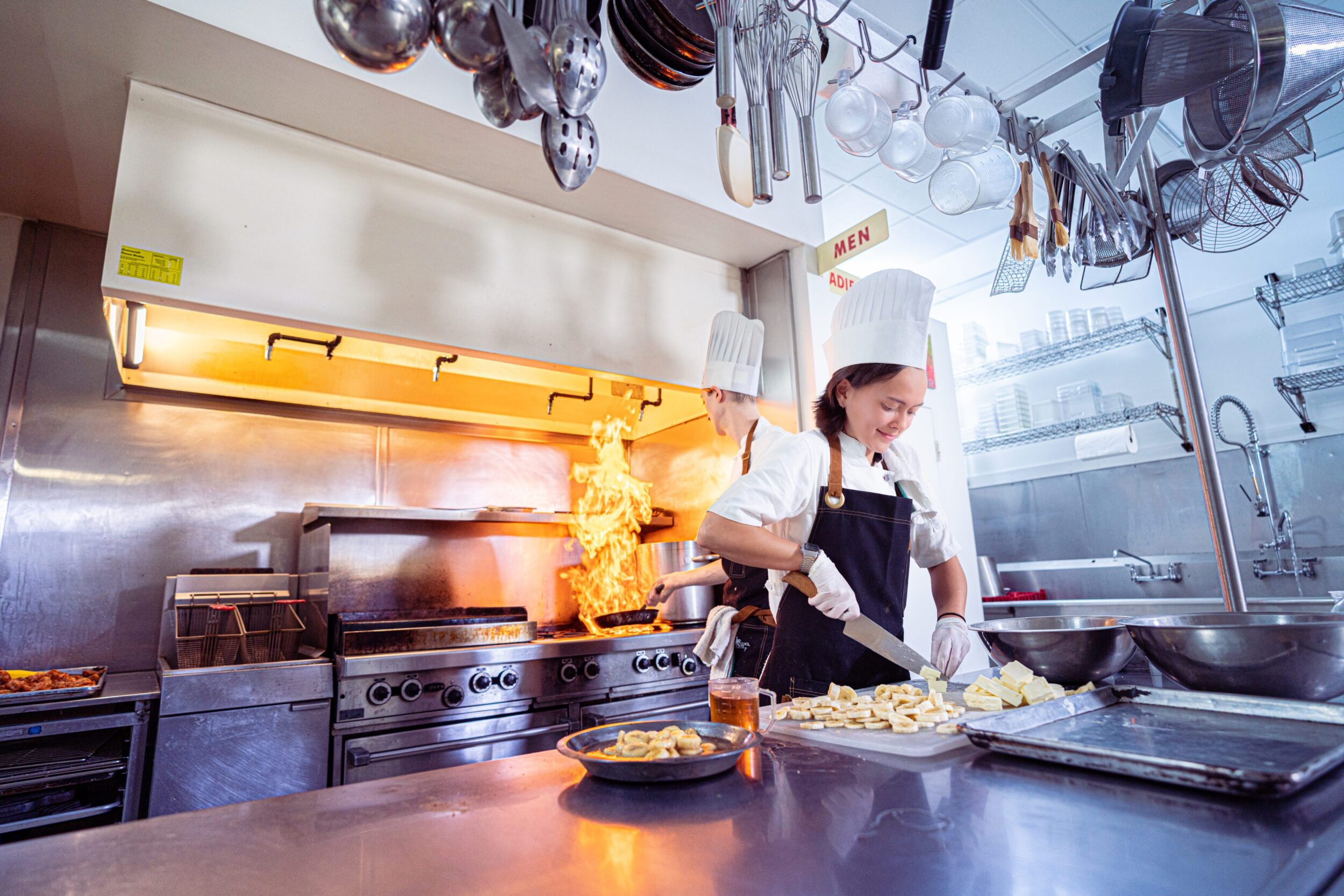 A young female chef wearing a black apron over white clothes and a white chef's hat. She works in a commercial kitchen located in Rocky Mount, VA.