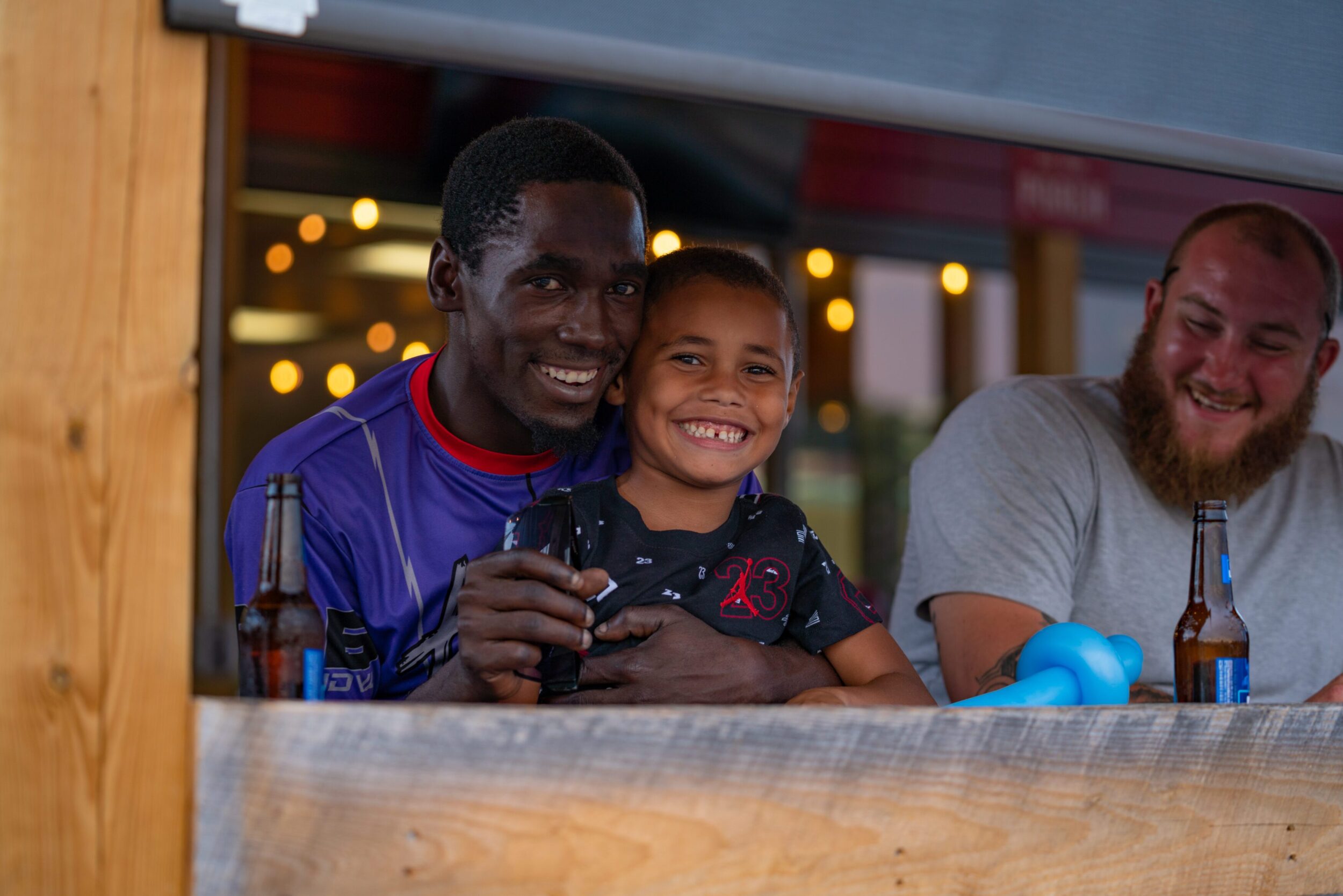 A Black father smiles at the camera as his son, also smiling, sits on his lap.