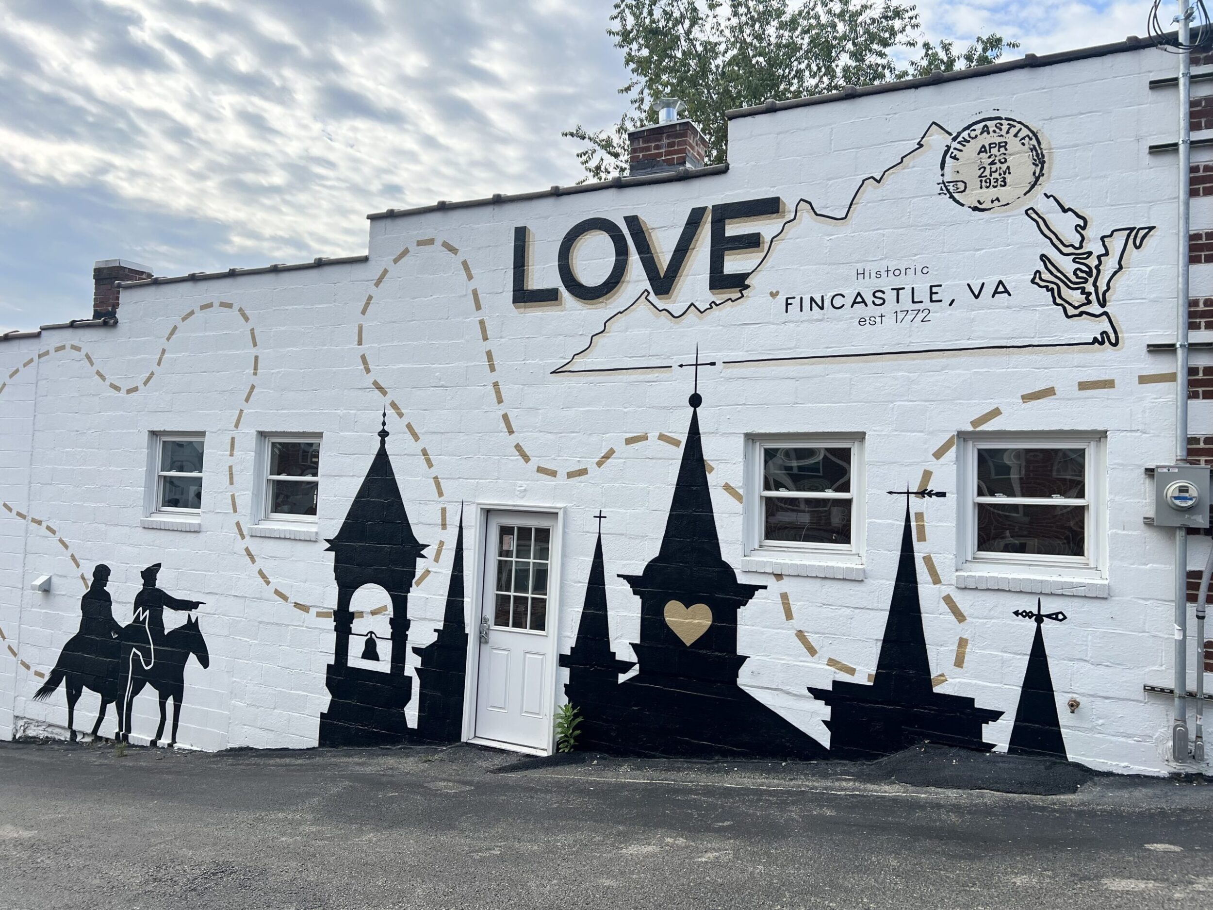 Mural on the side of a building in downtown Fincastle, VA. The building is white, and there are black building tops paints on the side with two silhouettes on horses, one of whom is pointing. Above the buildings is the outline of the state of Virginia with LOVE painted in black letter on the top left outside of the state's outline.